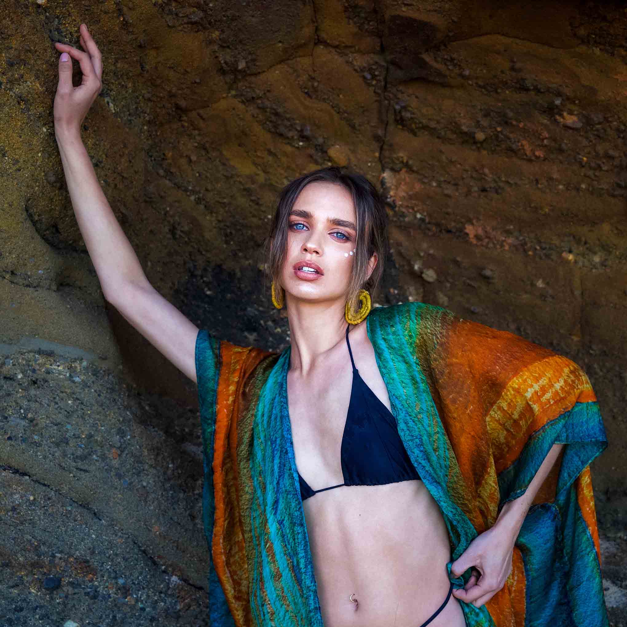 Woman in a Kamari kaftan and black bikini standing against a stone wall.